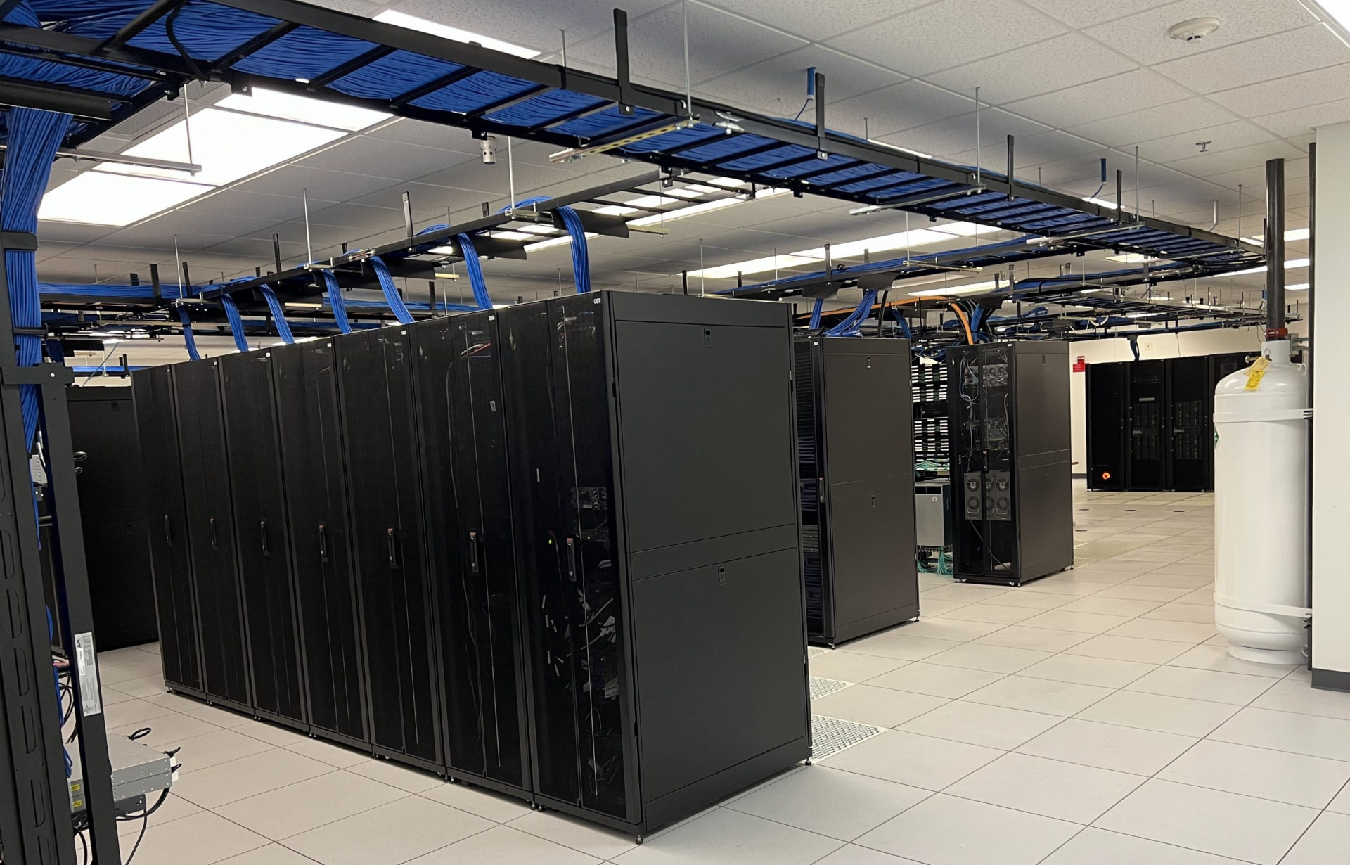 Rows of server cabinets beneath overhead cable trays in a data center